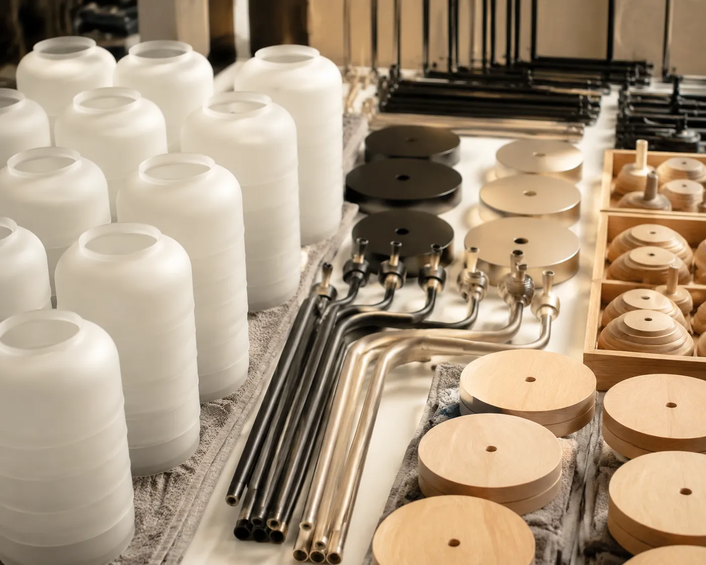 Glass shades, powder-coated steel arms and solid-wood bases staged in trays for assembly