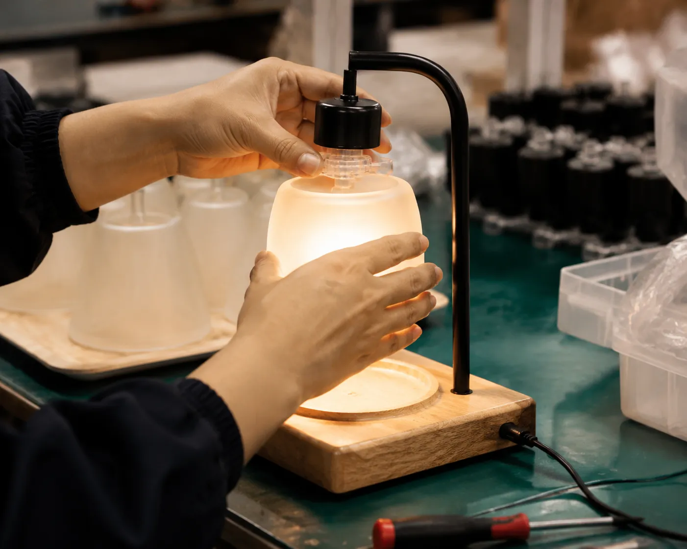A worker&rsquo;s hands assembling a candle warmer lamp at a lit assembly station
