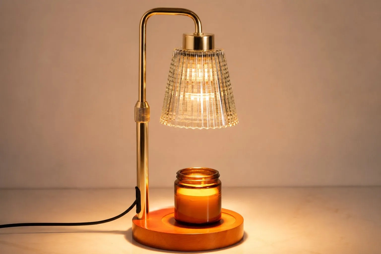 A warm-white candle warmer lamp with a glass shade and gold base lit over an unbranded candle on a neutral studio surface, ready for private-label packaging