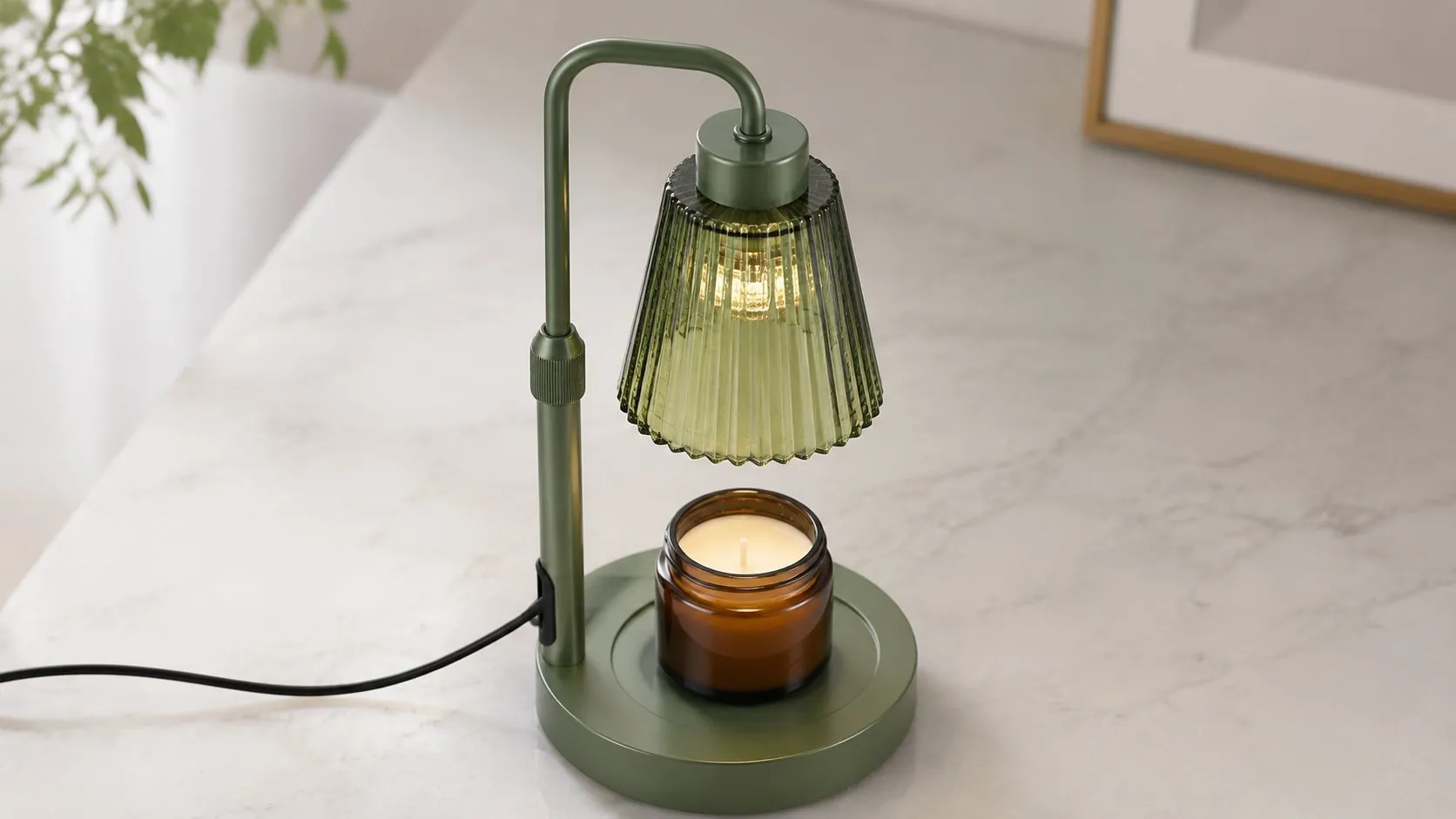 Sage-green candle warmer lamp seen from above, showing the glass shade housing the downward bulb over a jar candle, illustrating how a top-down candle warmer melts wax from the top