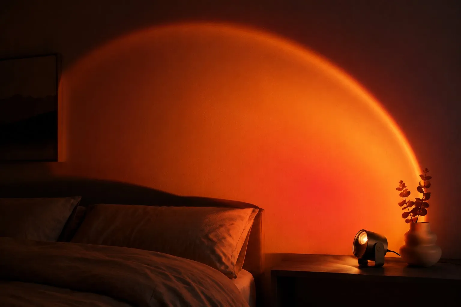 Sunset projection lamp casting a warm amber halo across a dark bedroom wall above a bed at night