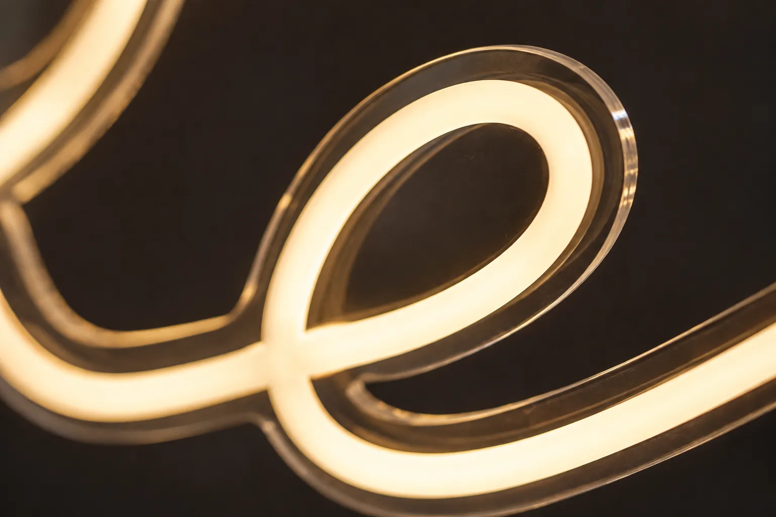 Close-up of a warm-white LED neon flex letter in a connected script on a clear acrylic backing, showing the continuous stroke and even tube thickness