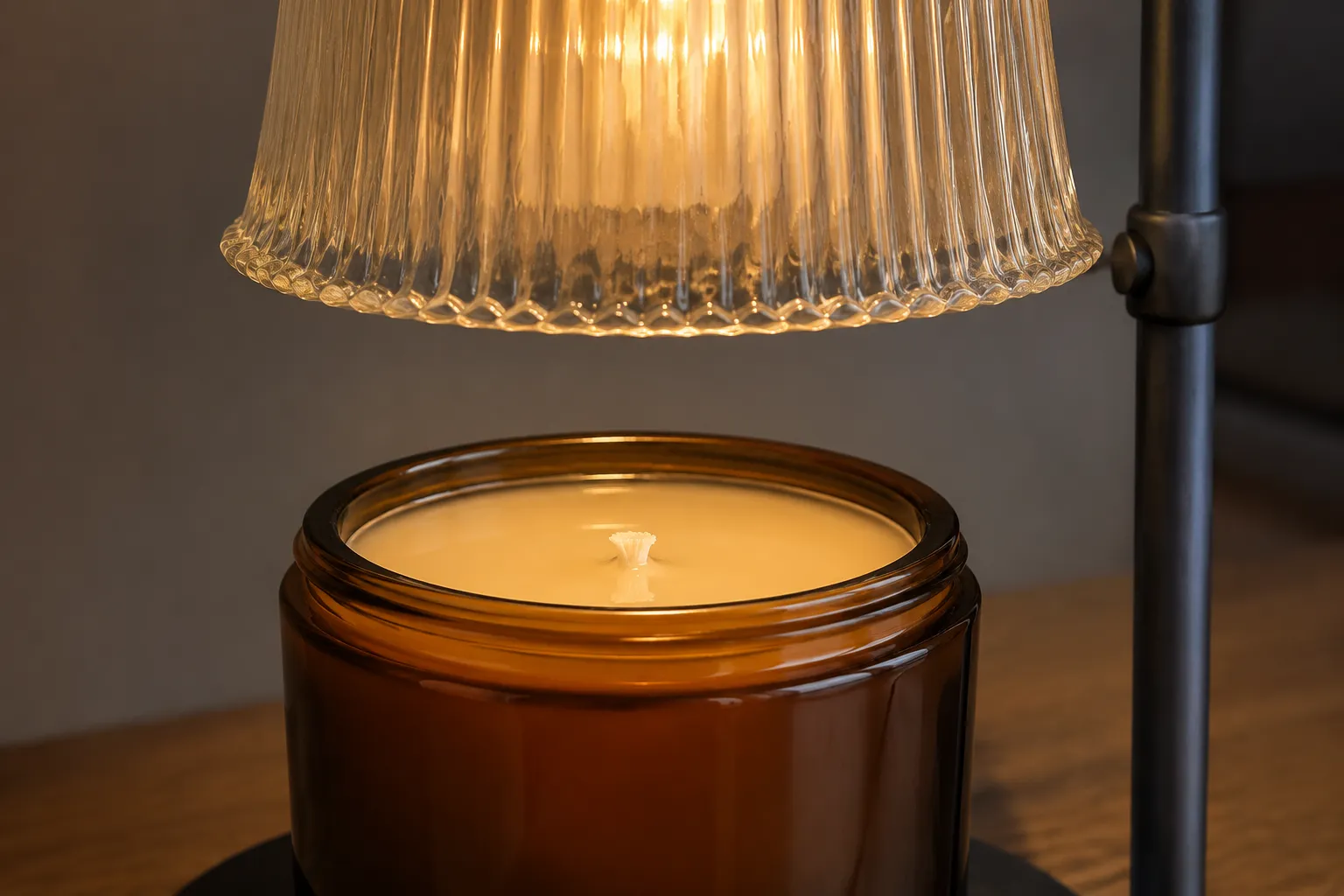 Top down candle warmer lamp with a glass shade suspended over an amber jar candle on a wooden side table, the wick unlit and a shallow melted pool across the wax surface