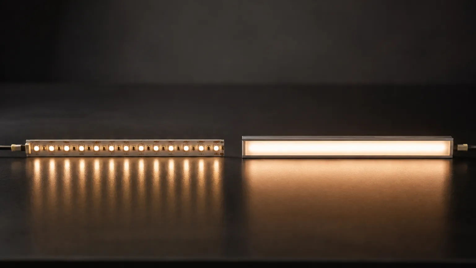 Two short lengths of LED tape lit side by side on a dark bench, one bare and showing individual diode dots, the other seated in an aluminum channel under a frosted cover as one continuous line of light