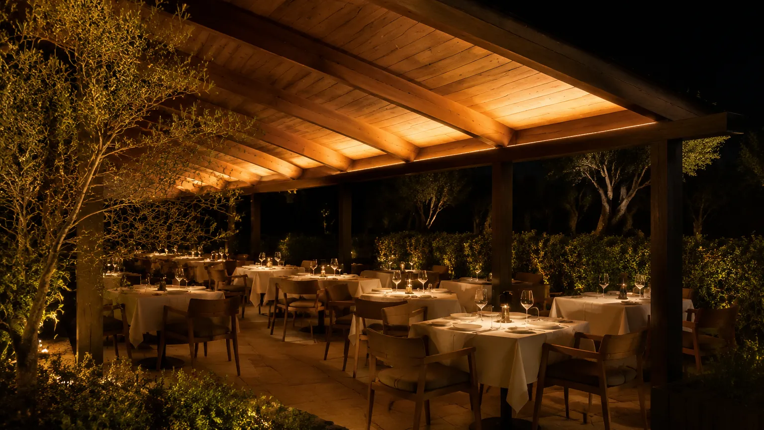 Restaurant terrace at night with a continuous concealed low-voltage LED strip washing the underside of a timber canopy above the tables
