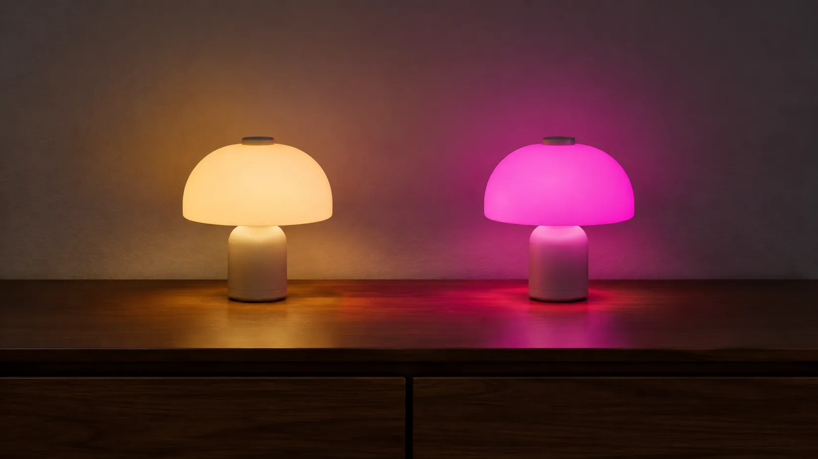 Two small decorative lamps side by side on a dresser, one glowing warm amber and one saturated magenta