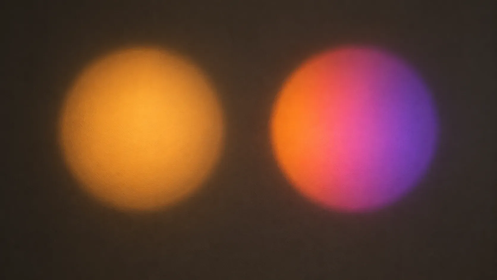 Two projected discs side by side on a pale wall, one plain warm amber and one graded through pink to violet