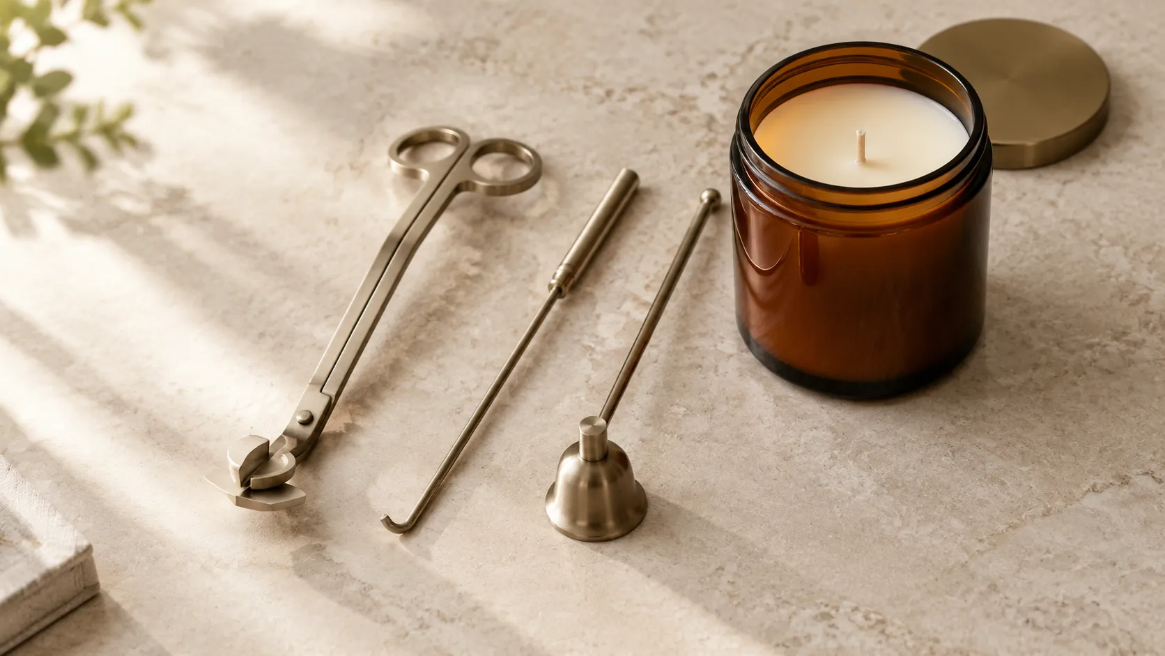 Three-piece candle care set, wick trimmer with angled blade, hooked dipper and bell snuffer, beside an unlit jar candle