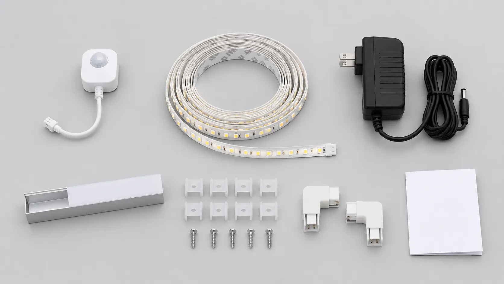Flat lay of a cabinet LED strip kit: coiled white strip, sensor module, plug-in adapter, mounting clips and channel