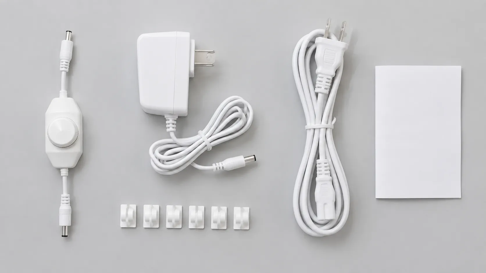 Low-voltage adapter, inline dimmer and cable clips arranged on a plain surface beside a coiled white power lead