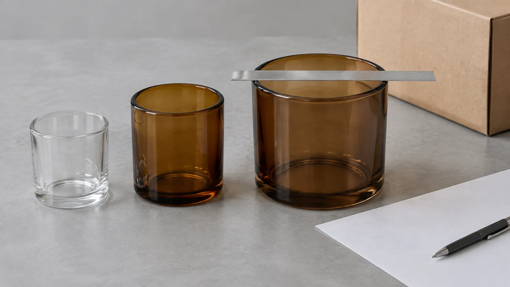 Three unlit glass candle jars of different widths on a buyer desk with a steel ruler measuring the inside diameter of one