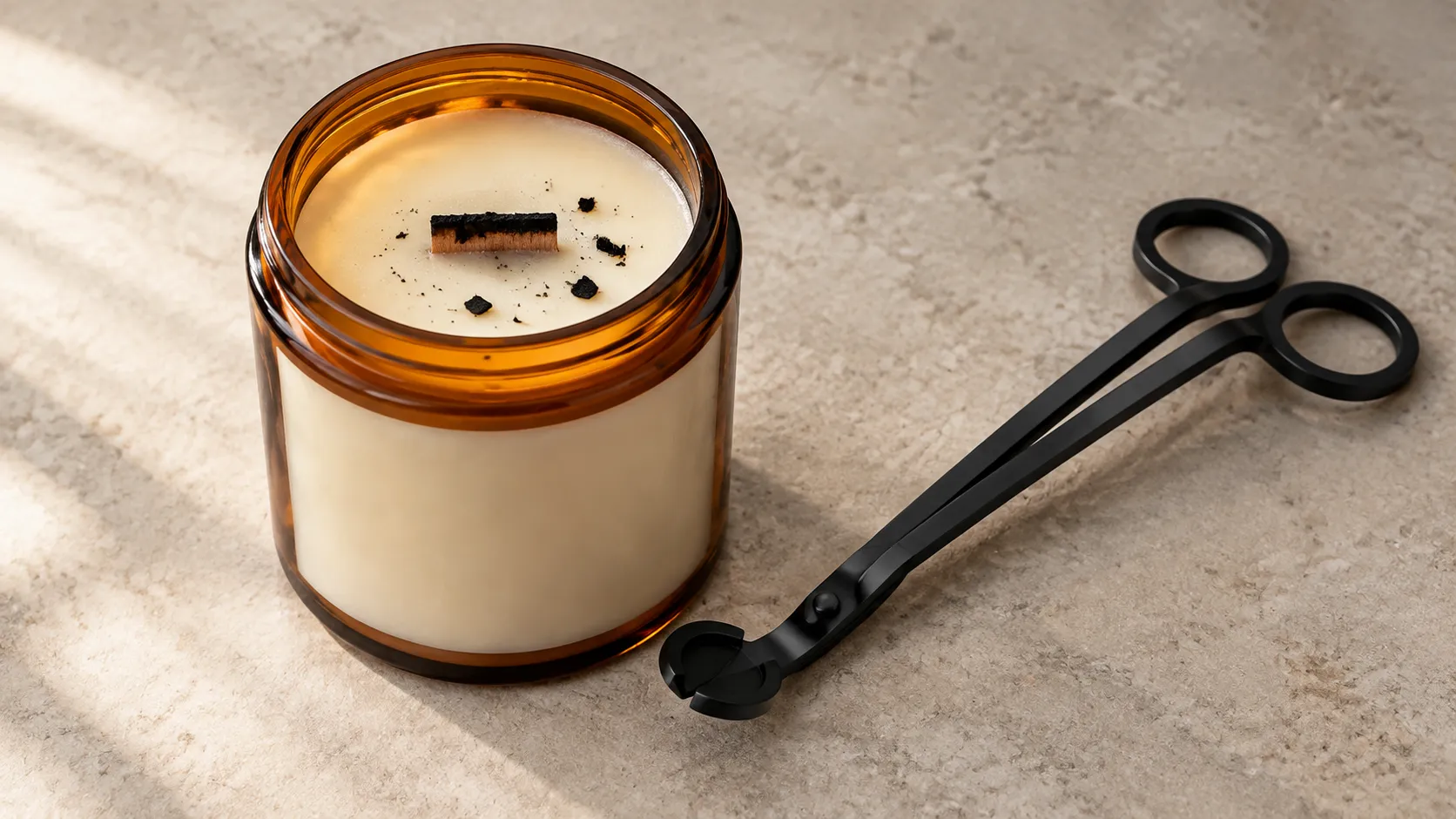 Cold wooden wick candle with a charred crust across the wick and dark wood flakes on the wax surface, trimmer alongside