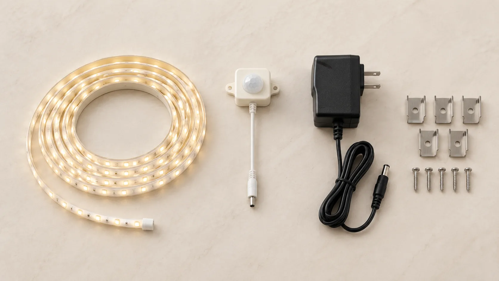 Under-cabinet motion-sensor LED strip kit laid out flat with coiled strip, sensor, driver, clips and screws