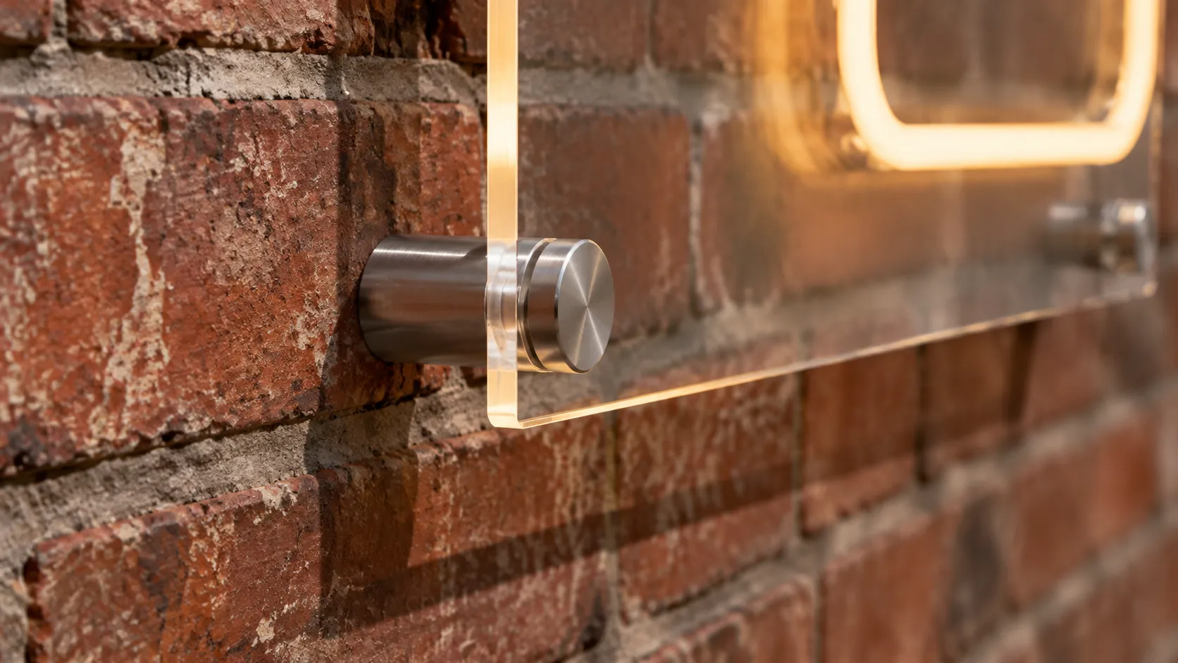 Close view of a clear acrylic sign backboard held off an old brick wall on four metal standoff barrels