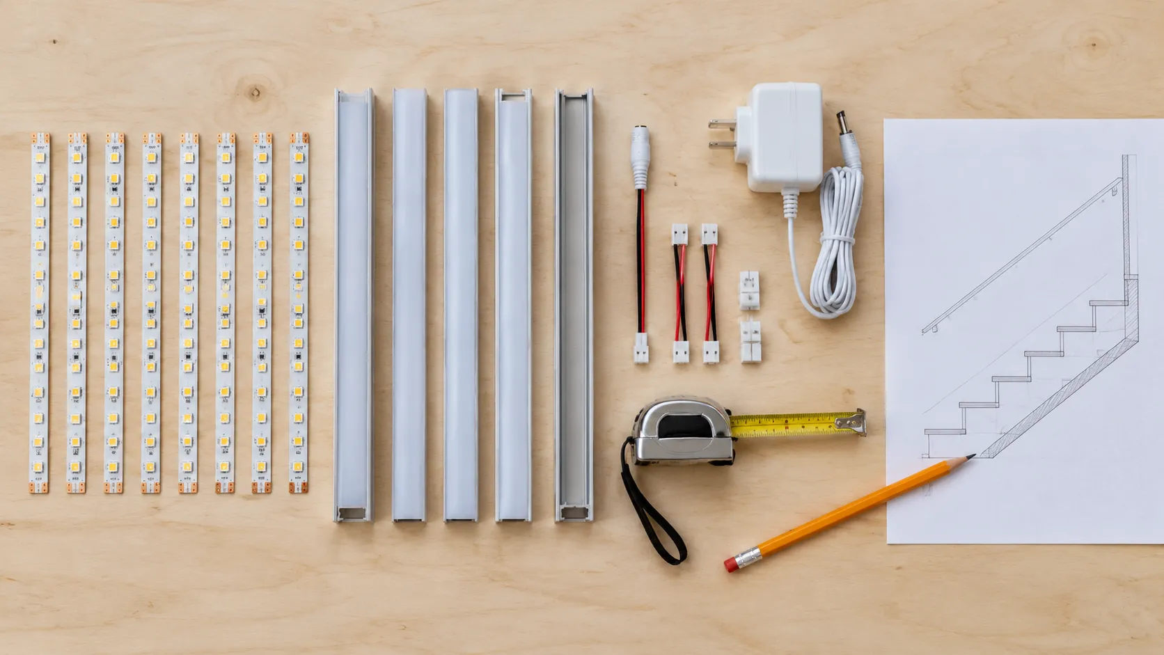 Flat lay of a stair strip order: pre-cut tape segments, aluminium profiles with frosted covers, leads and adapter