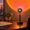 Black desk sunset projection lamp with a metal swivel joint casting an orange sunset glow on the wall