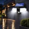 Dual-head solar motion-sensor light with a top solar panel on a dark grey wall beside a garage door at night