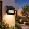 Black solar flood light with a hinged top solar panel mounted on a white villa wall at dusk