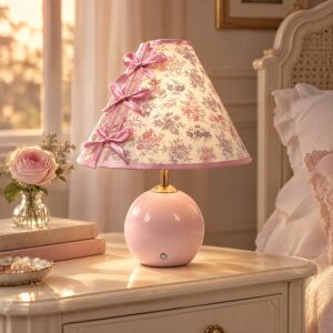 Pink ceramic ball-base bedside lamp with a gold-tone stem and cone-shaped floral shade on a cream nightstand