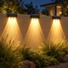 Three solar wall wash lights casting warm V-shaped beams down a rendered garden wall