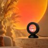 Black round-lens sunset lamp on a low domed base casting an orange sunset circle on a living-room wall